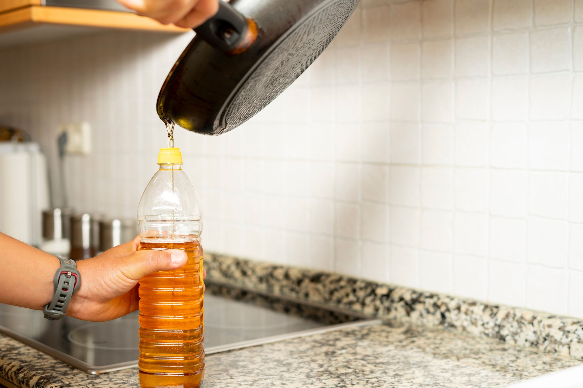 Close up of a man's hands recycling edible oil from a frying pan into a plastic bottle in his home kitchen